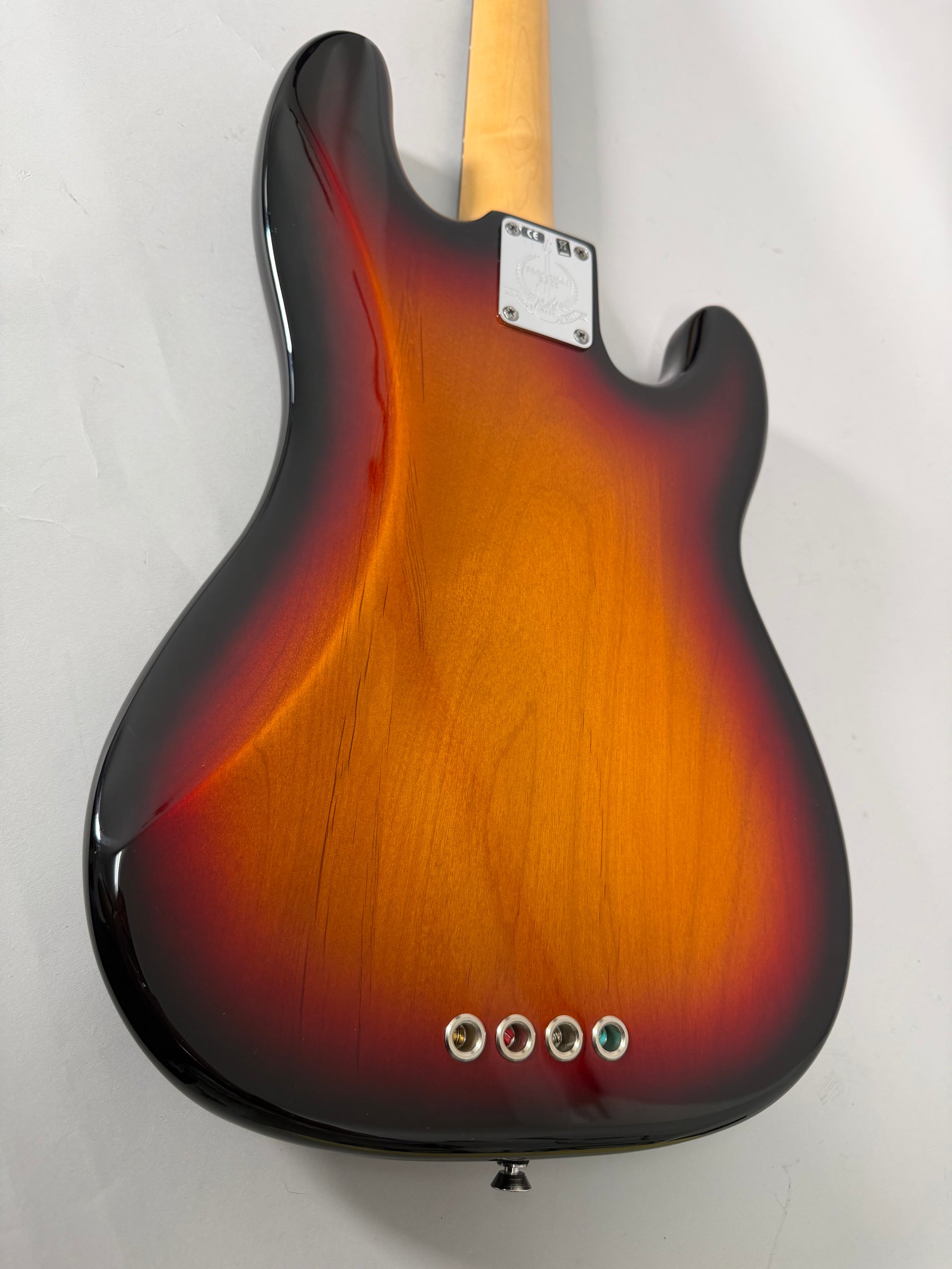 The bass guitar's sunburst back shows a glossy finish, a chrome neck plate, and four string ferrules near the bottom edge.