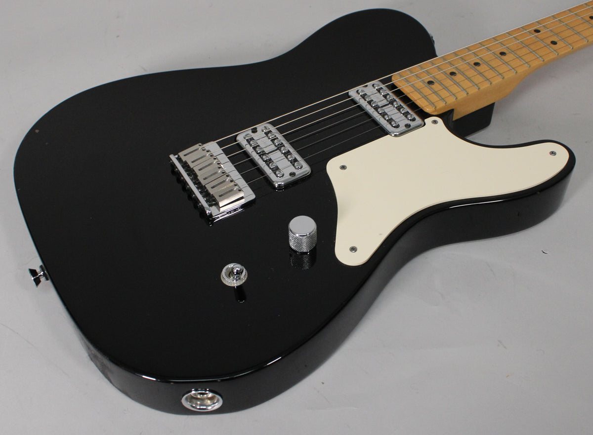 Black solid-body electric guitar, angled from the lower bout, with a cream pickguard, two chrome humbuckers, and a maple neck.