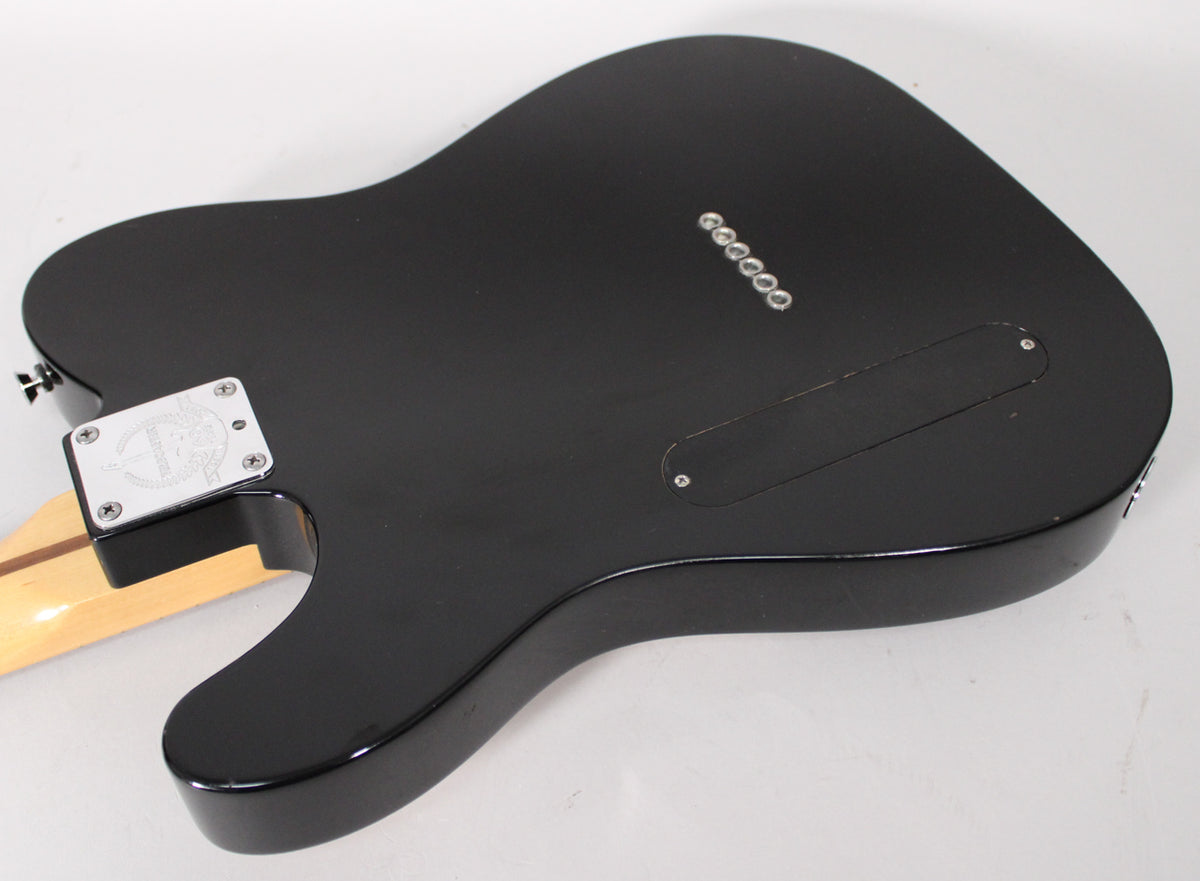 The black electric guitar's back shows a satin finish, a chrome neck plate, and six string-through-body ferrules.