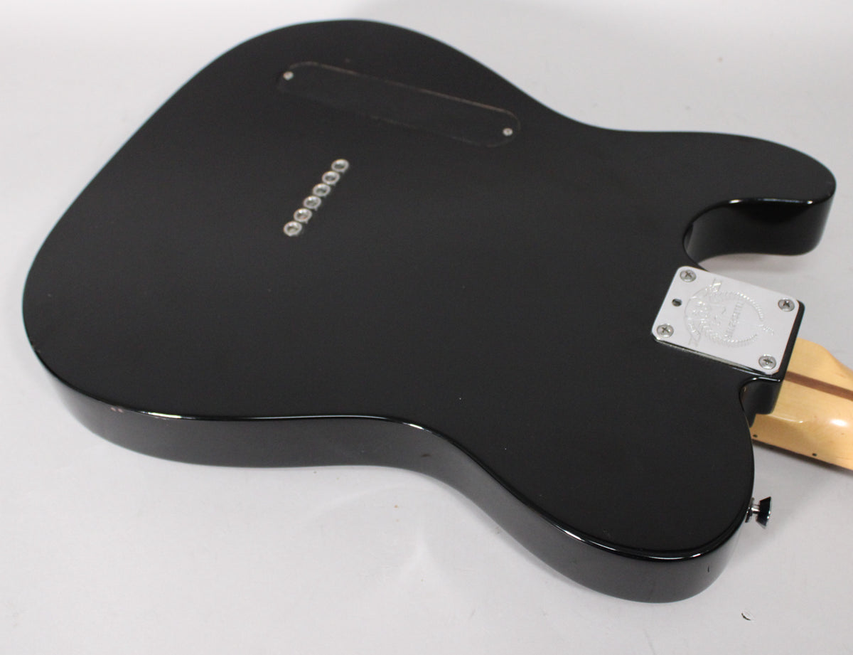 The black guitar body is viewed from the back, showing a satin finish, chrome string-through ferrules, and a silver neck plate.