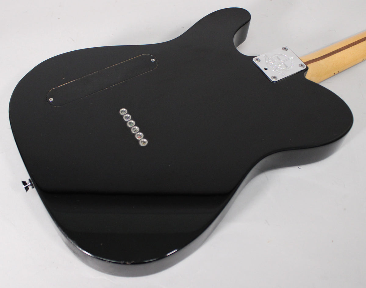 The guitar's black body, with a matte finish on top and gloss on the bottom, shows its back with a chrome neck plate and string-through ferrules.