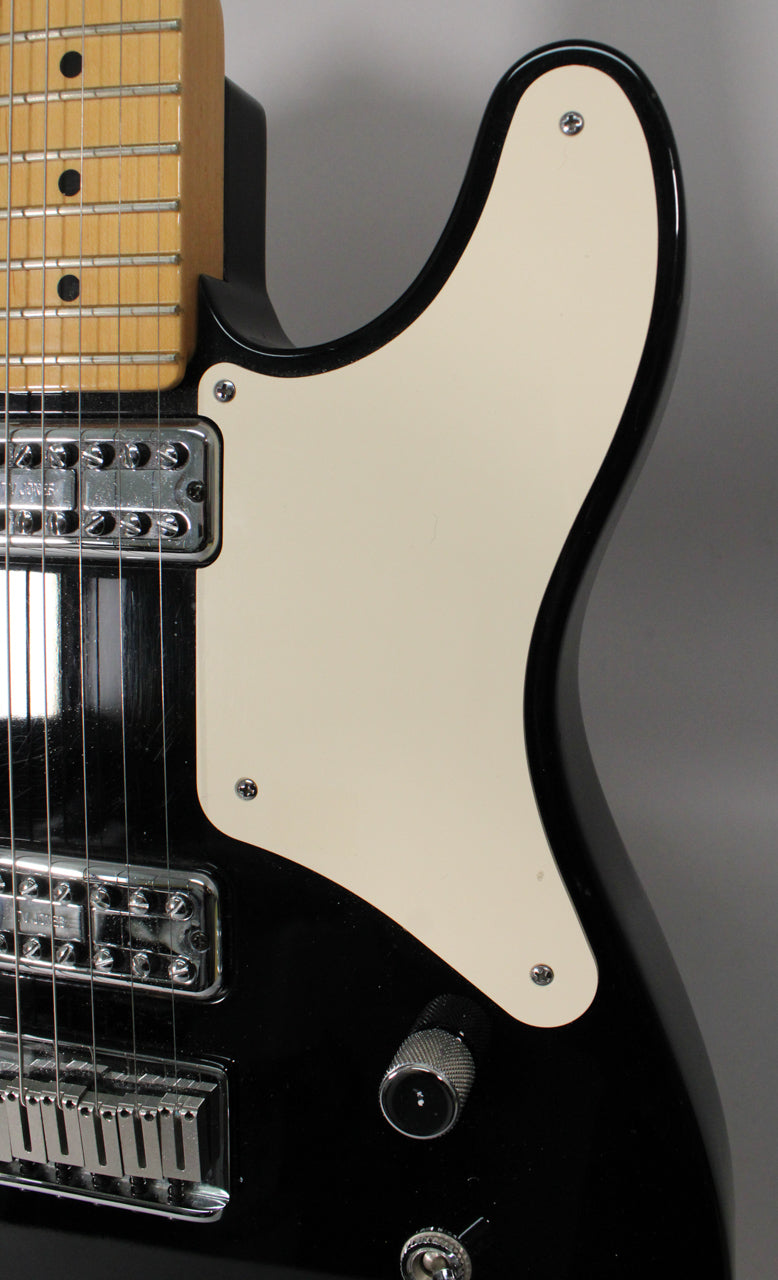 Close-up of the black guitar body, showing the cream pickguard, two chrome humbucker pickups, a chrome bridge, and two chrome control knobs.