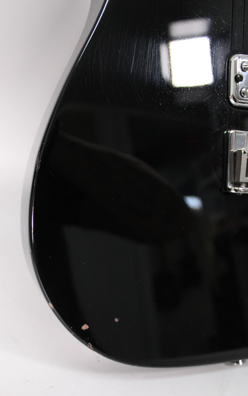 Close-up of the glossy black body, showing many light scratches, a small chip on the edge, and two small paint chips near the bottom.
