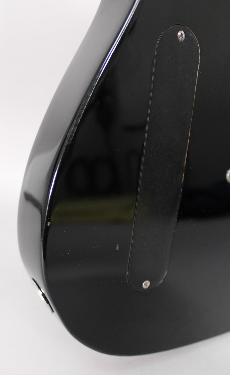The black guitar body's lower bout is shown from the back, with a long, narrow control cavity cover and output jack.