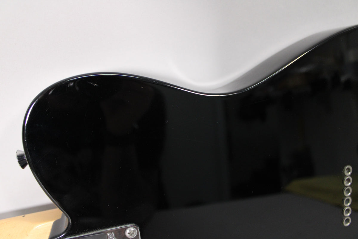 Close-up of the black gloss body's upper bout, showing light scratches and the six string-through-body ferrules.