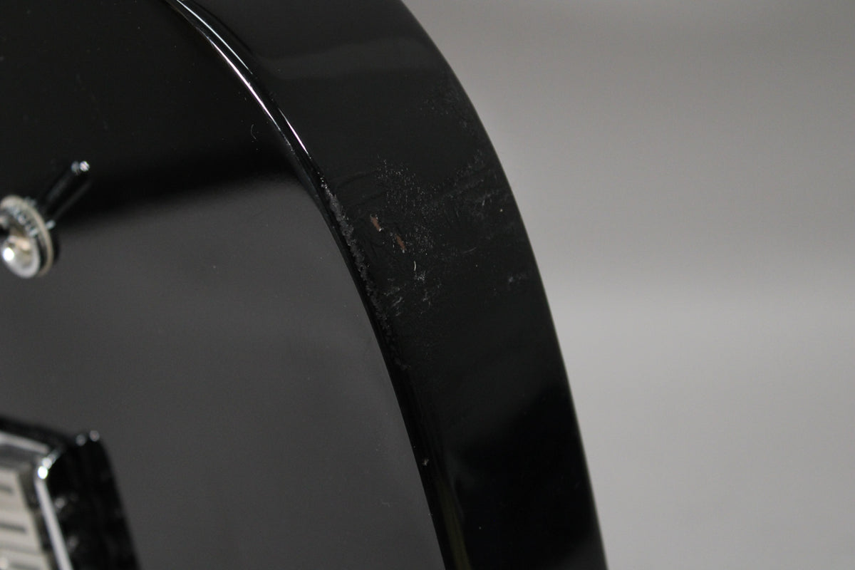Close-up of the black guitar body's curved edge, showing several small chips and scuffs in the glossy finish.