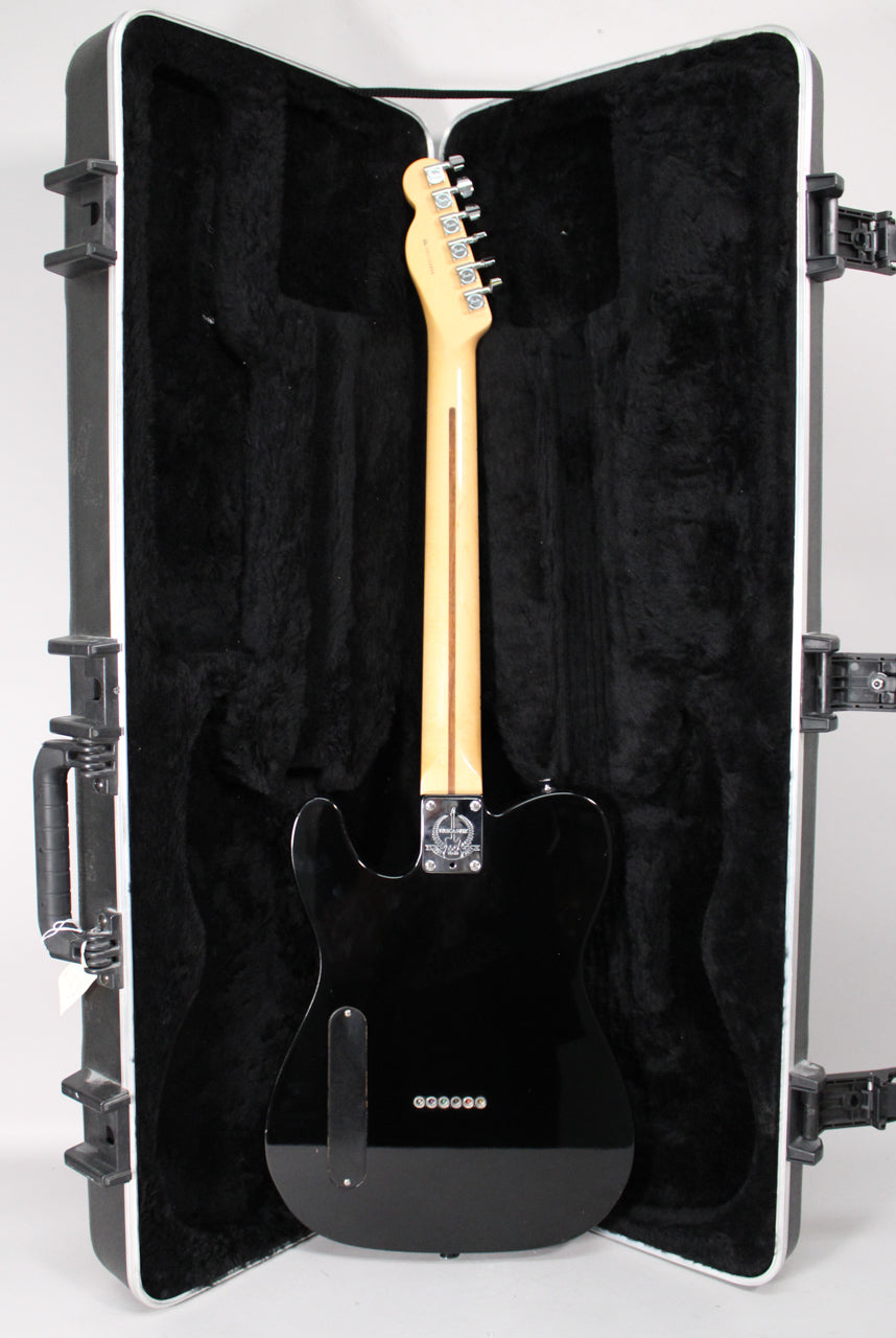 The black Telecaster is shown from the back, resting in its open hard case, revealing a light maple neck and chrome hardware.