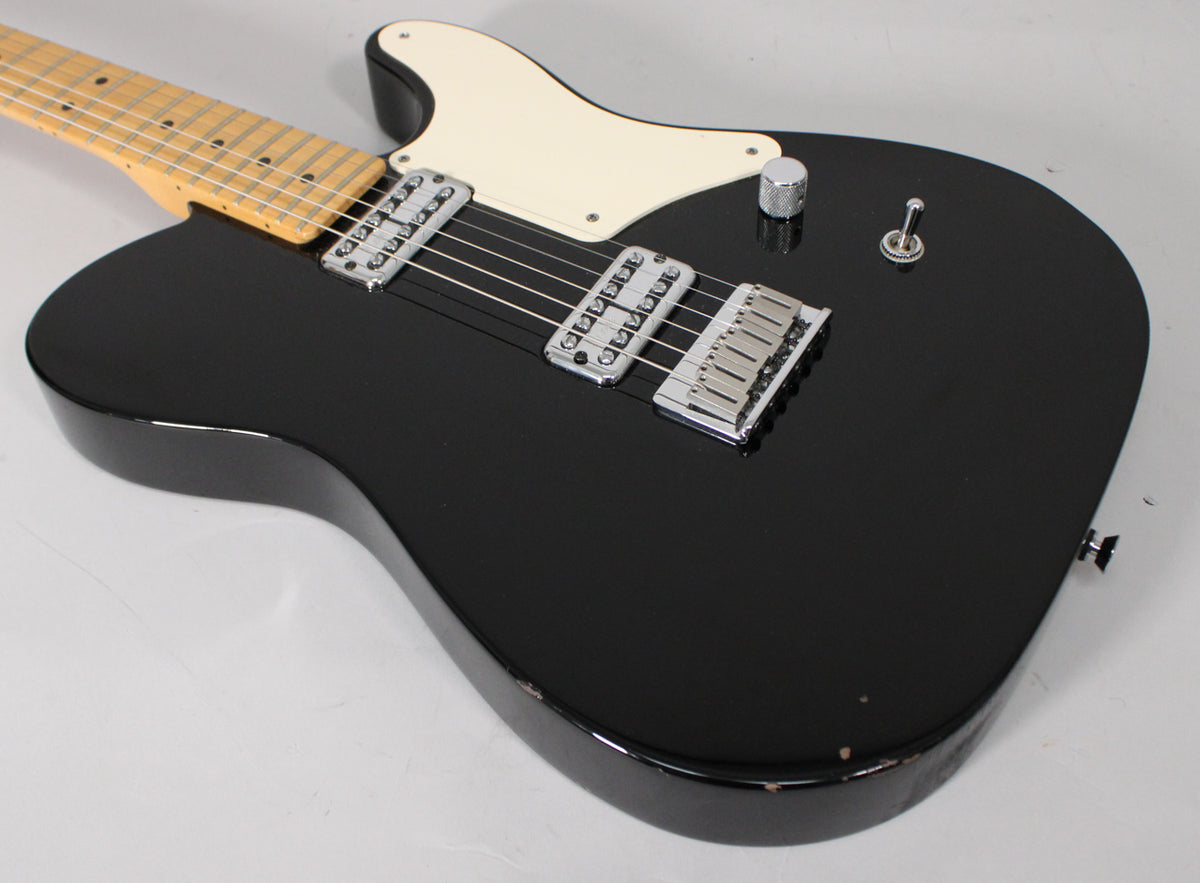 Black electric guitar, angled view of the body and lower neck, with a cream pickguard, two chrome humbuckers, and a single volume knob.