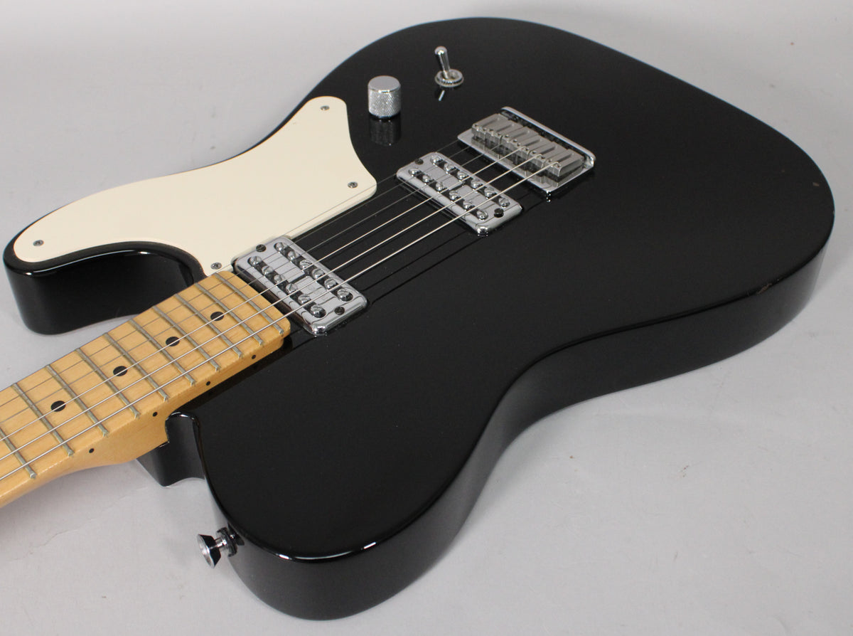 Close-up of a black electric guitar with a maple neck, two chrome humbuckers, a single volume knob, and a three-way toggle switch.