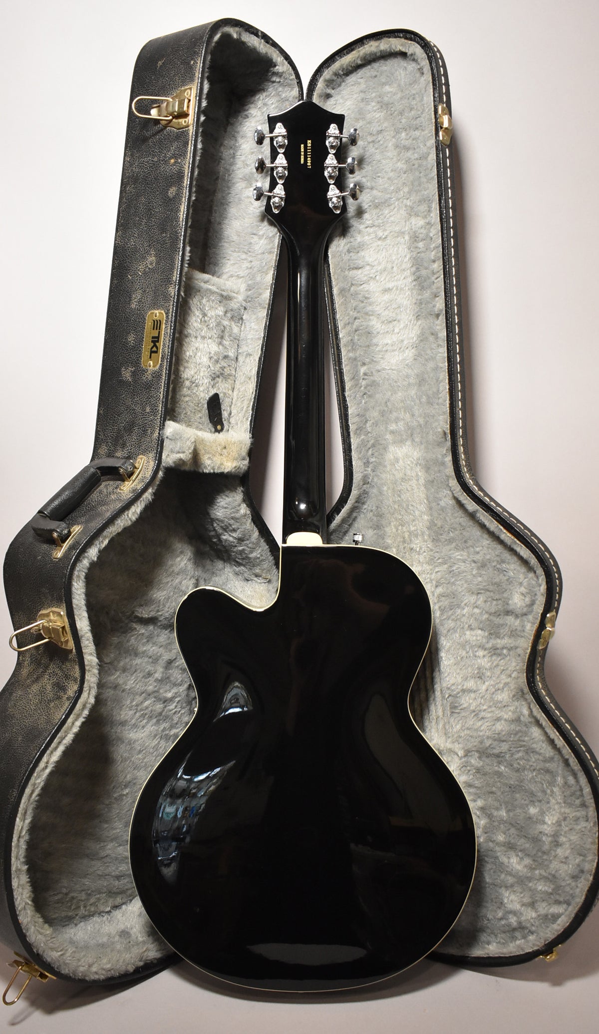 The black hollowbody electric guitar is shown from the back, with its headstock and neck resting in a grey-lined open hard case.