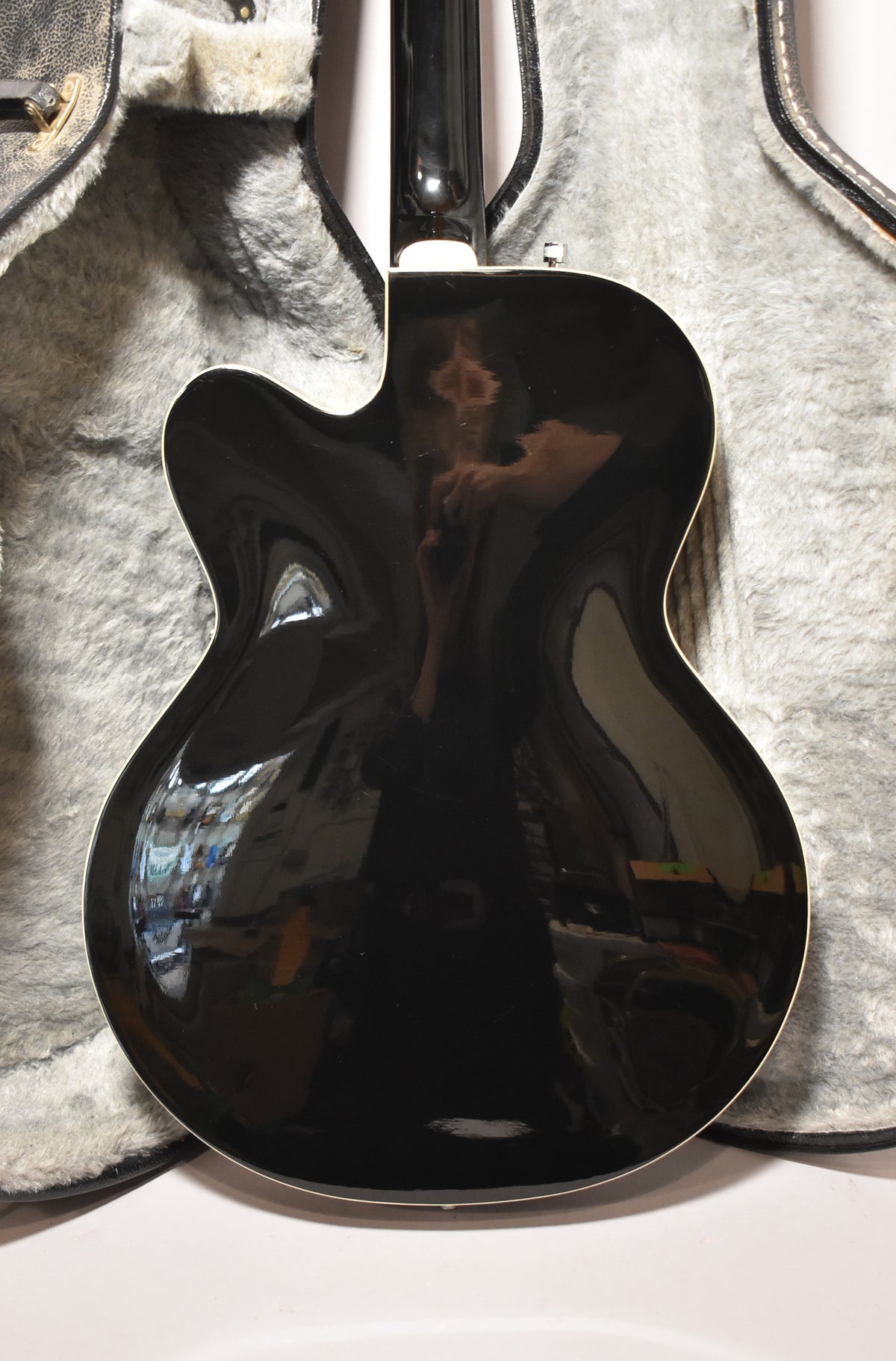 The black hollowbody guitar's back is shown, with a glossy finish reflecting the room, and a white binding around the body.