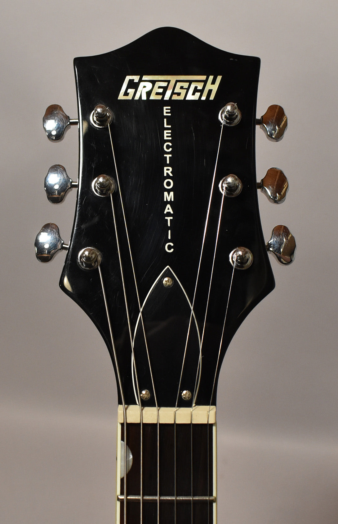Close-up of the black headstock with six chrome tuners, showing light scratches and a white nut above the dark fretboard.