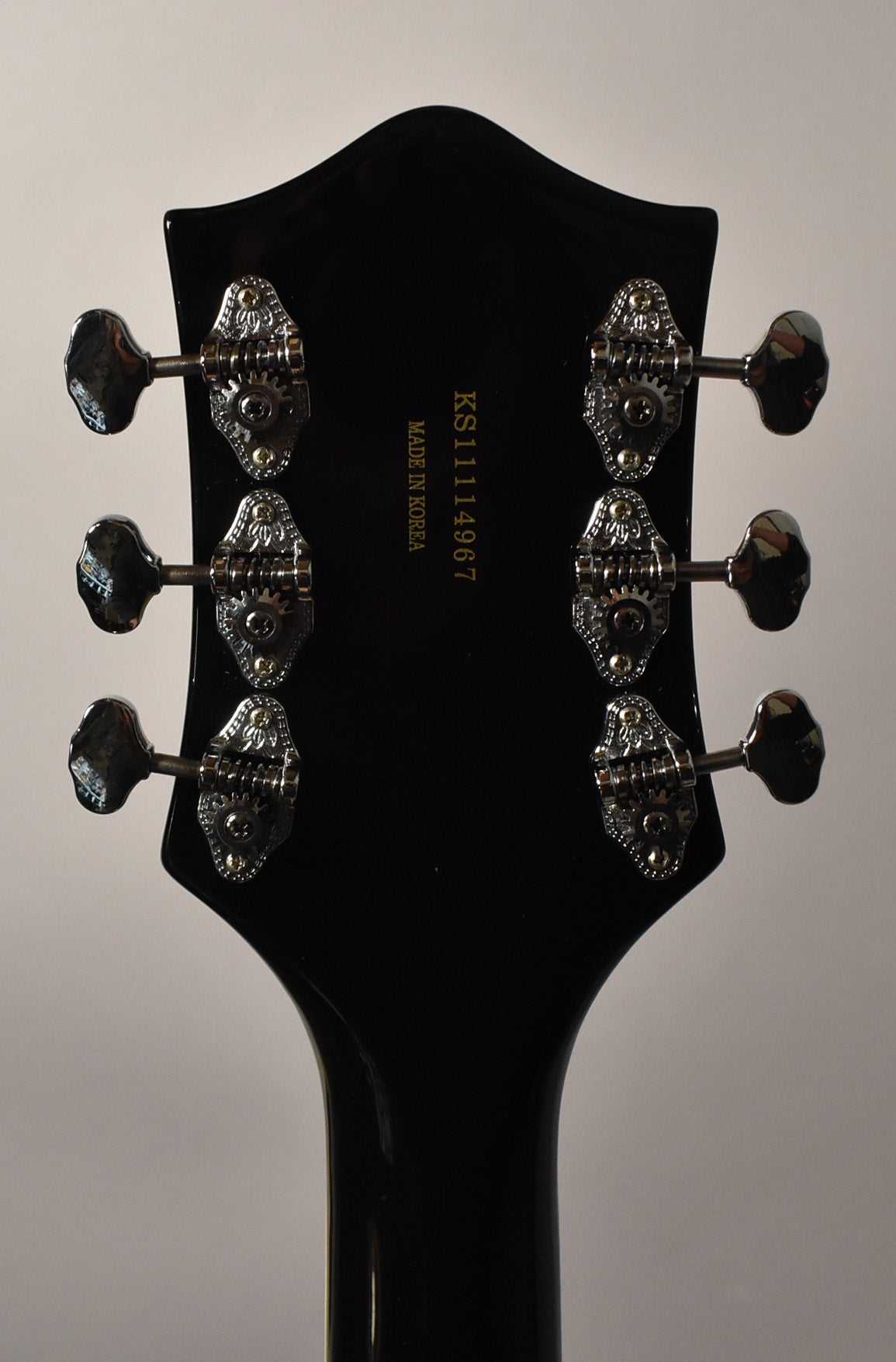 Rear view of the black gloss headstock and neck, showing six chrome open-gear tuners with ornate plates and black buttons.