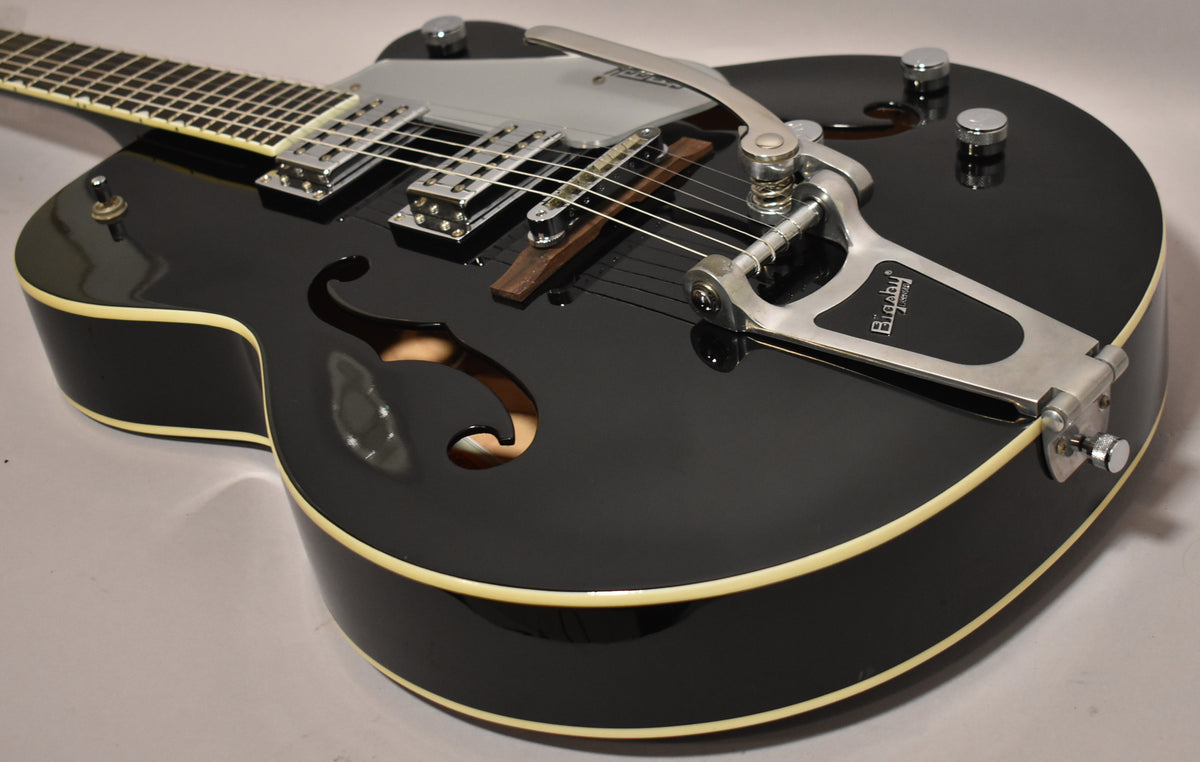 Black hollowbody electric guitar, angled view of the body, showing cream binding, f-holes, chrome Bigsby tremolo, and two humbuckers.