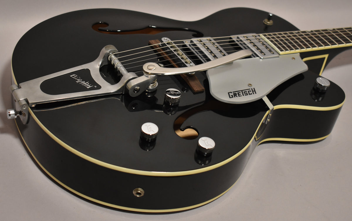 Black hollowbody electric guitar, angled view of the body, showing the Bigsby vibrato, pickups, and control knobs.