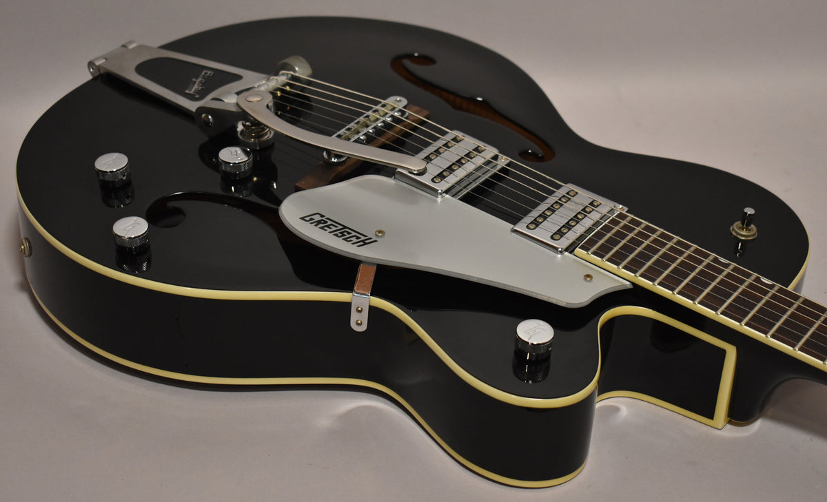 Black hollowbody electric guitar, angled from above, showing the Bigsby tremolo, two humbuckers, and silver pickguard.