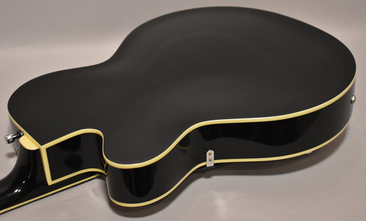 The guitar's black matte back and glossy sides are visible, with cream binding along the edges and a strap button on the lower bout.