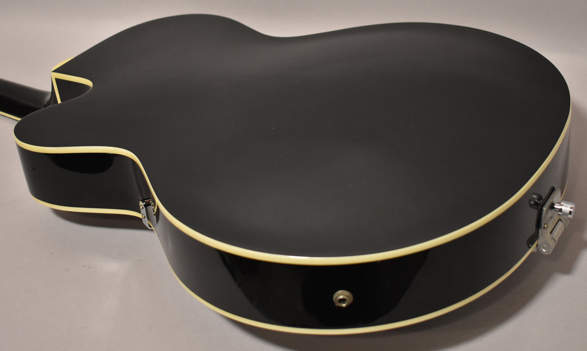The black hollowbody guitar's back and side are visible, showing cream binding, a matte finish on the back, and a glossy finish on the side.