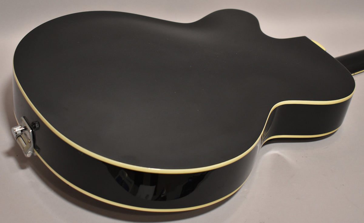 The black hollowbody guitar's back and side are shown, with cream binding and a chrome strap button visible on the lower bout.