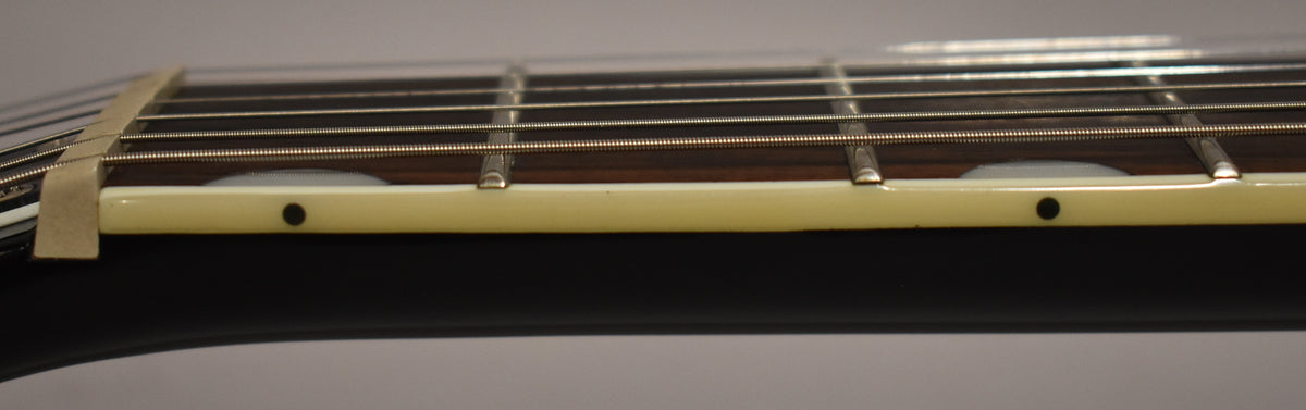 Close-up of the black guitar's fretboard from the side, showing the nut, frets, strings, and cream binding with black side dots.