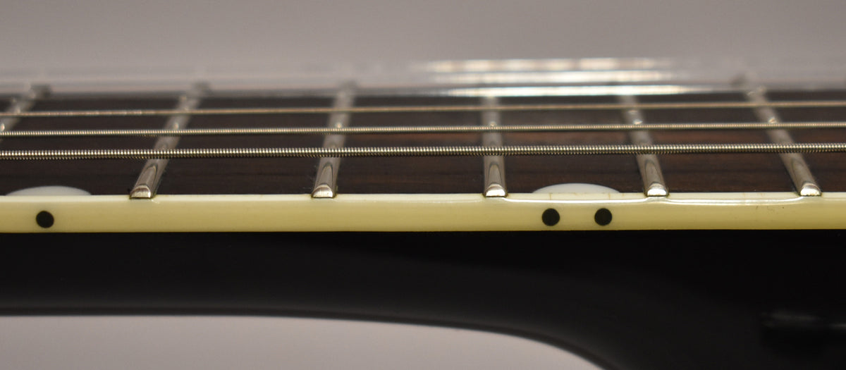 Close-up of the guitar's dark fretboard and frets, with cream binding and black side dots, viewed from the bass side.