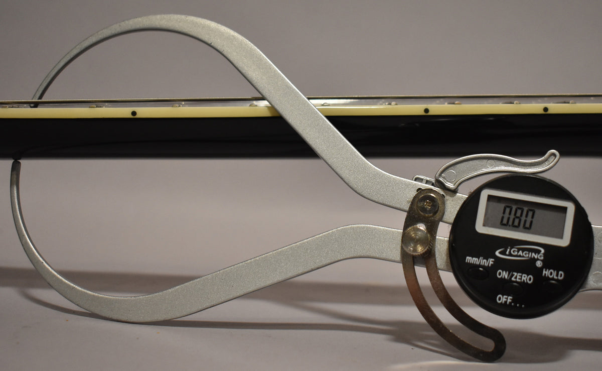 A digital caliper measures the guitar's black neck and cream binding, showing "0.80" on its display.