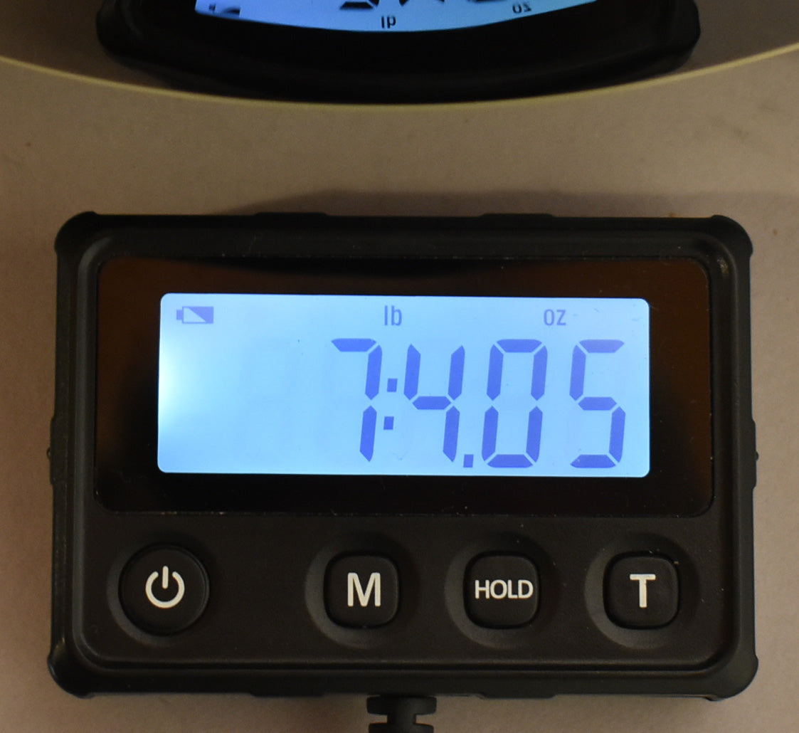 Close-up of a digital scale displaying "7:14.05" in blue light-up numbers, indicating the guitar's weight in pounds and ounces.