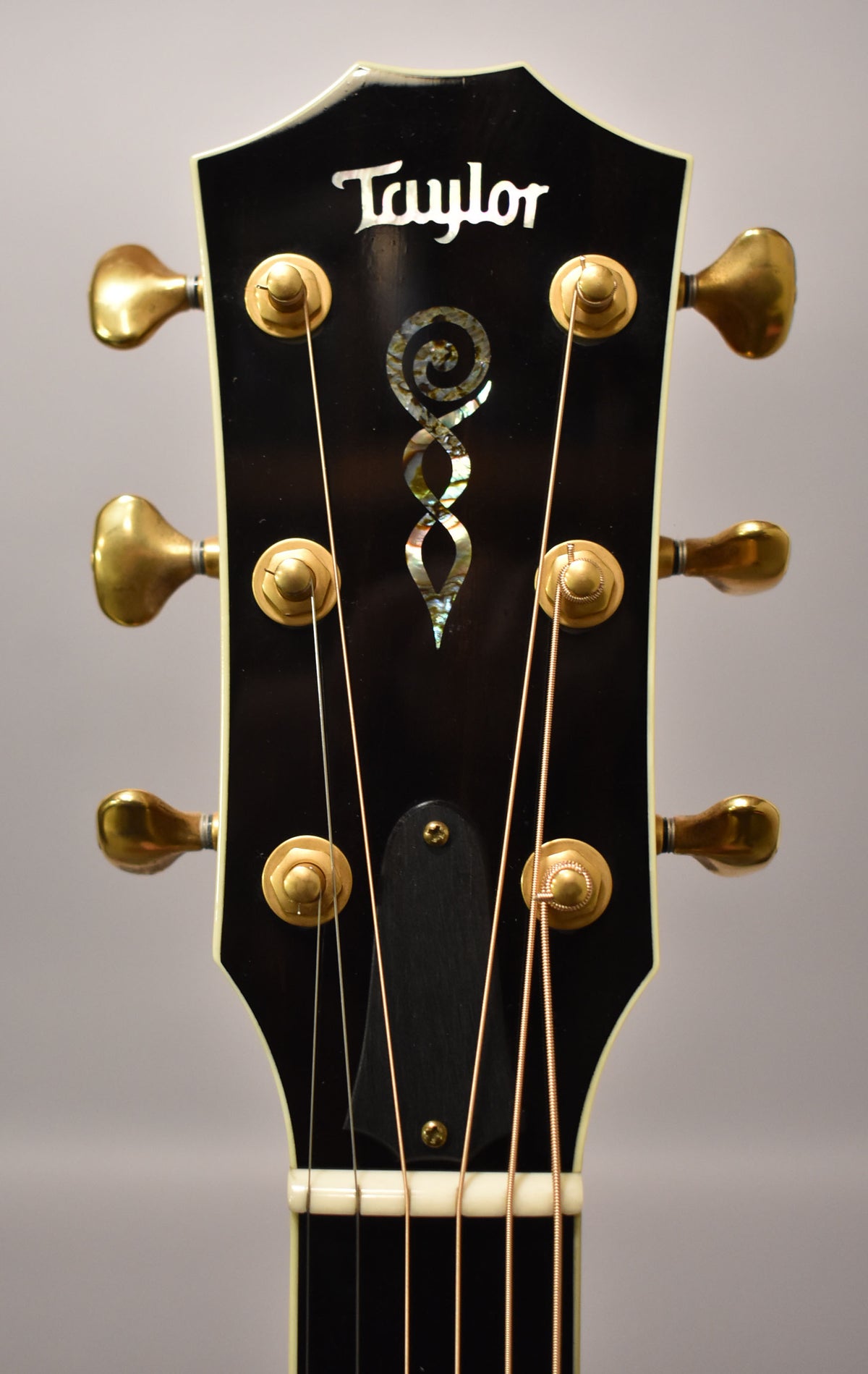 Close-up of the glossy black headstock with gold tuners and a mother-of-pearl infinity symbol inlay, showing some light wear.
