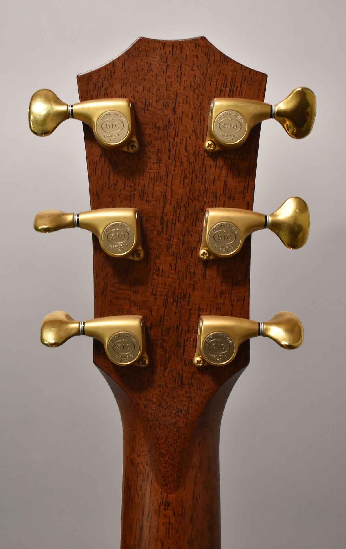 The back of a mahogany headstock and neck, with six gold-plated tuning machines arranged 3x3, showing light wear.
