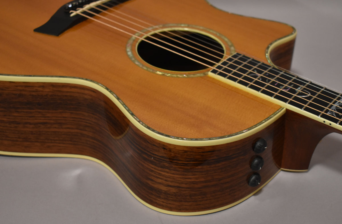 The natural finish acoustic guitar's body and neck are angled, showing the dark wood grain sides and three black control knobs.