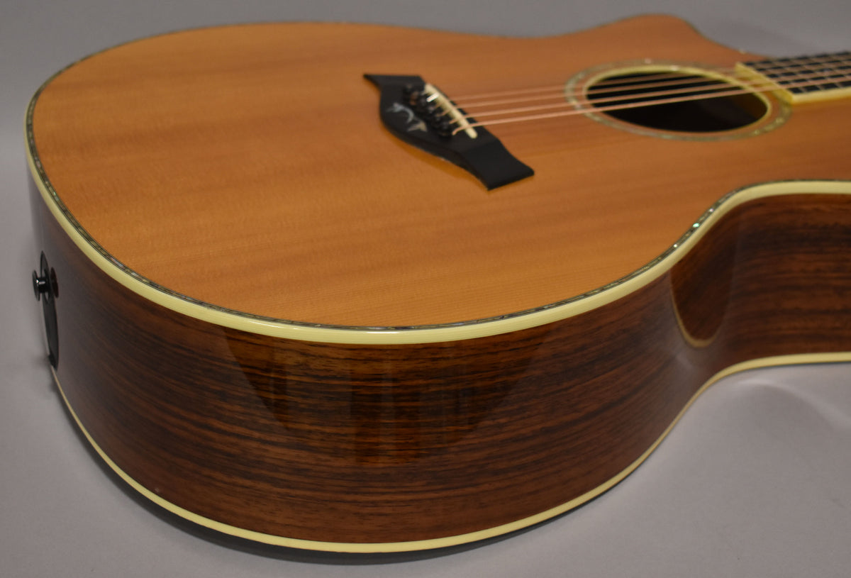 The acoustic guitar's natural wood top and dark, glossy sides are visible from the lower bout, with an output jack on the side.