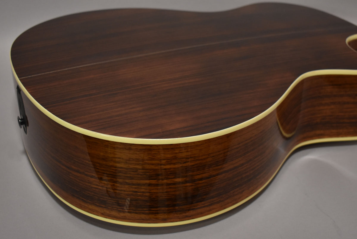 The acoustic guitar's dark brown, glossy back and side are visible, with a cream binding and a black endpin jack.
