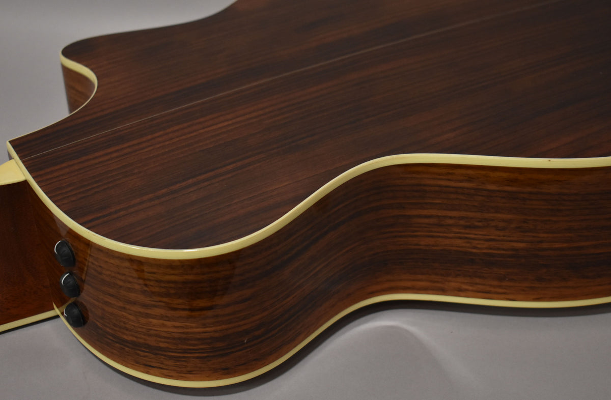 Close-up of the guitar's lower bout and cutaway, showing the dark, striped wood grain of the back and sides with cream binding.
