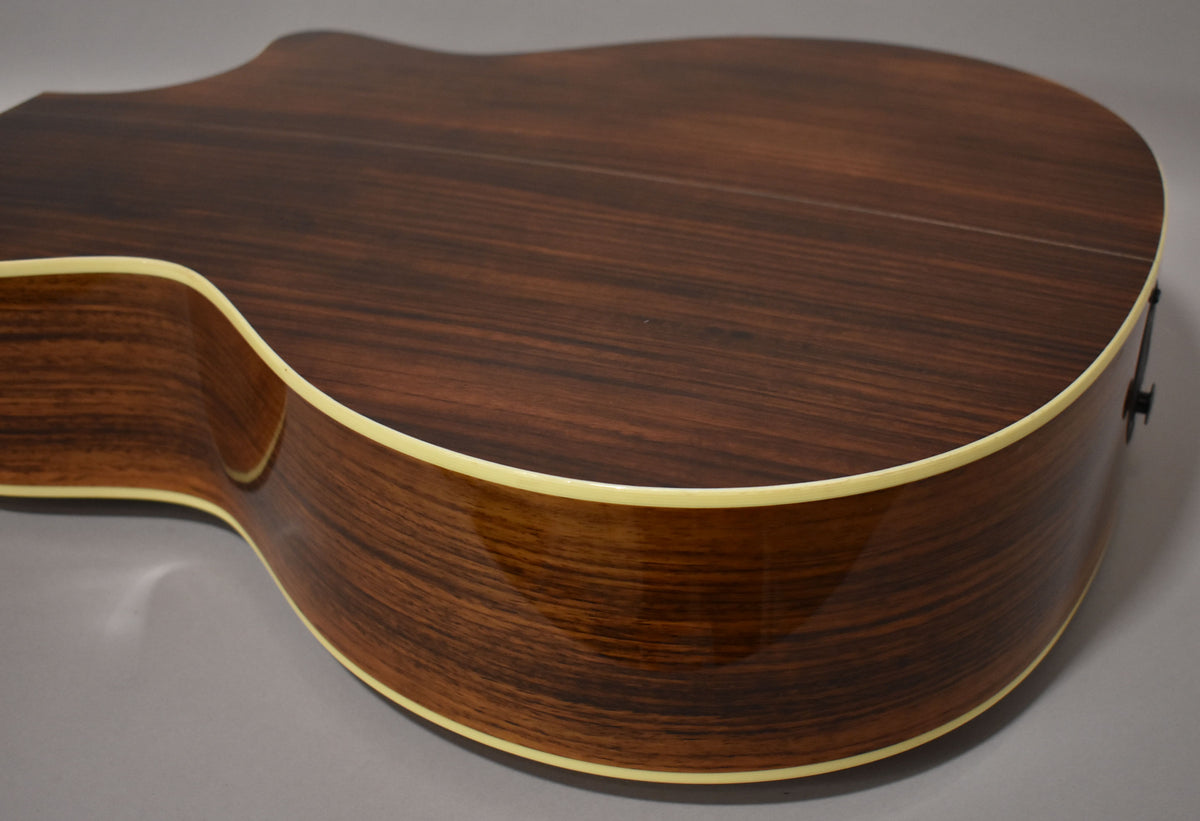 The guitar's dark wood back and side are shown from the lower bout, with light binding and a visible output jack.
