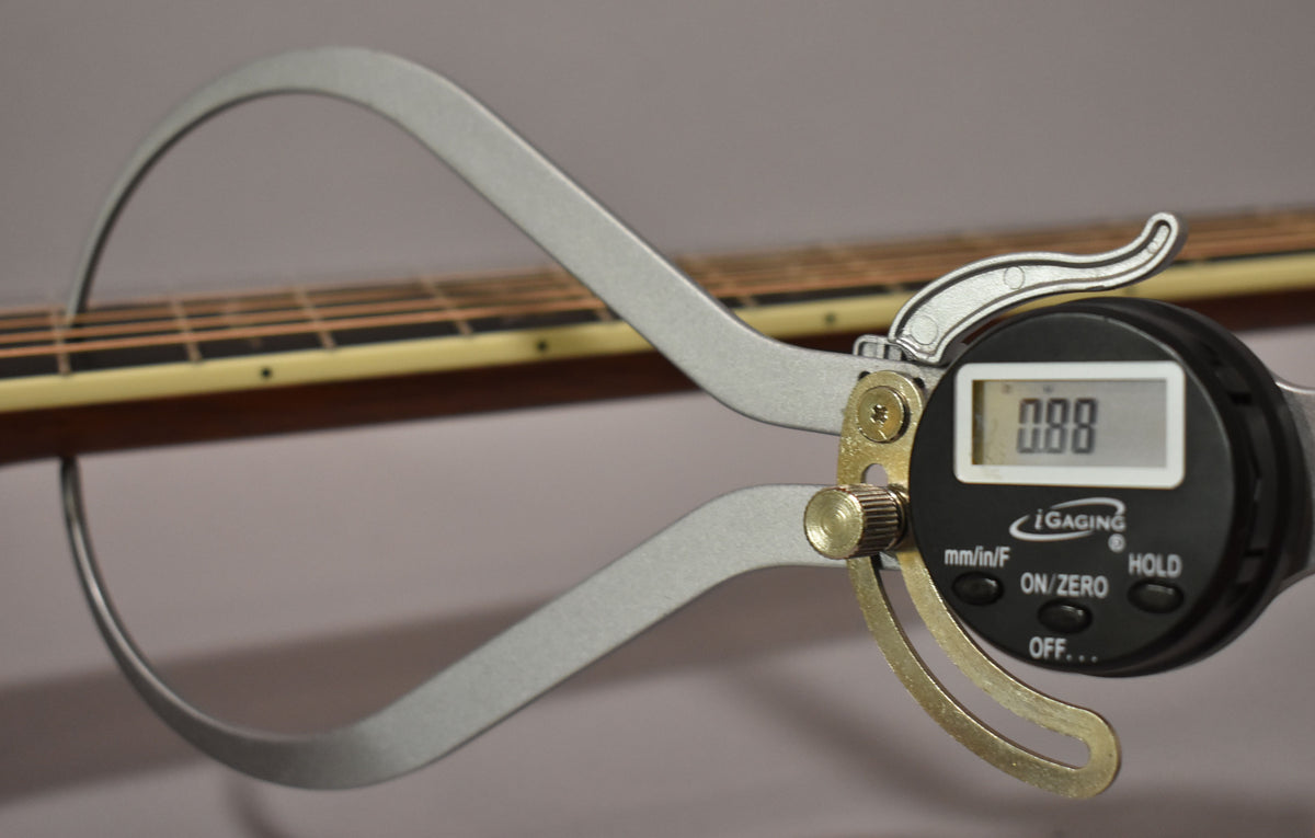 A digital caliper measures the guitar's fretboard and strings, showing "0.00" on its display.