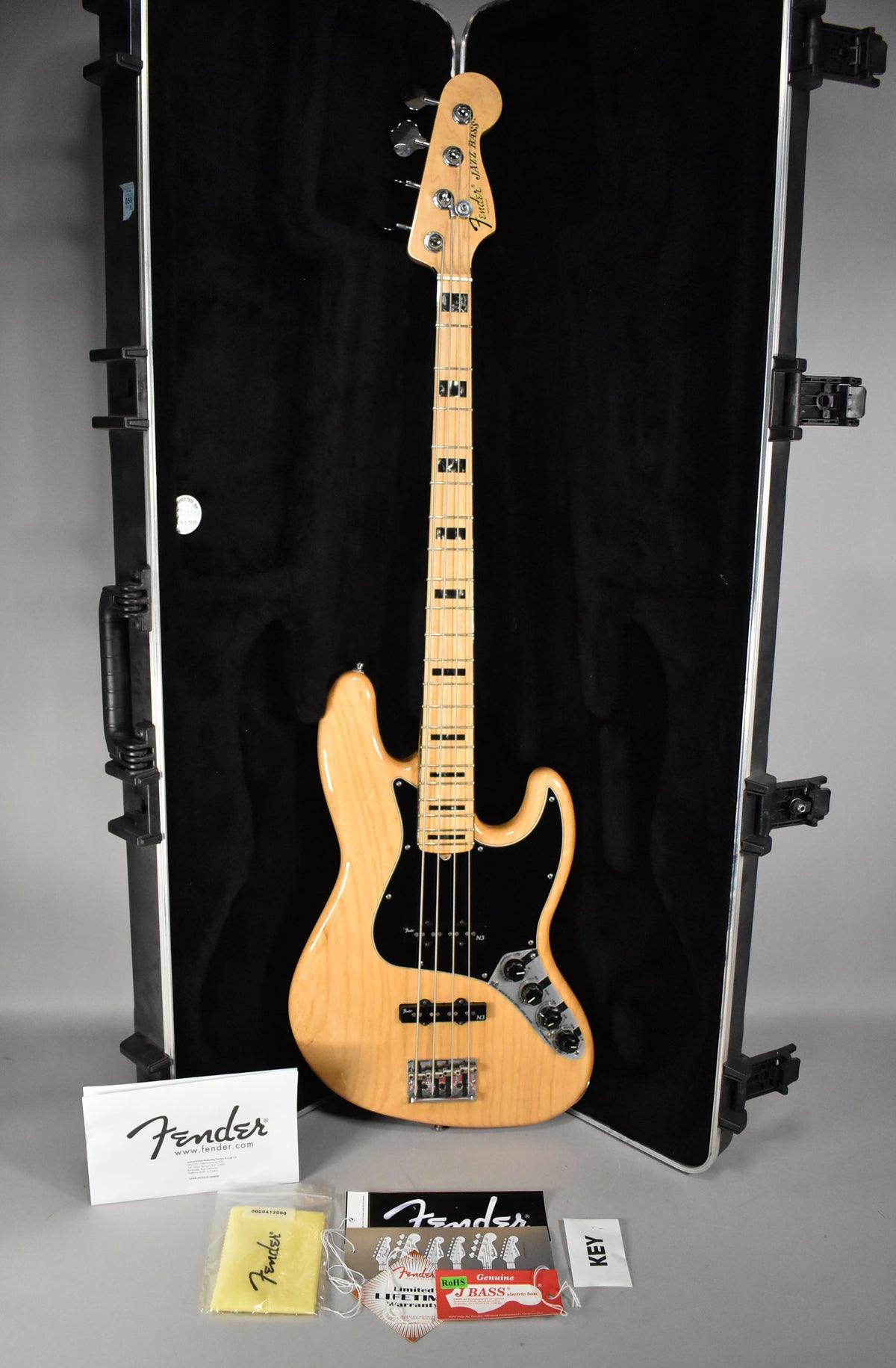Full-length view of a natural finish Jazz Bass with a black pickguard, block inlays, and chrome hardware, resting in its open hard case.