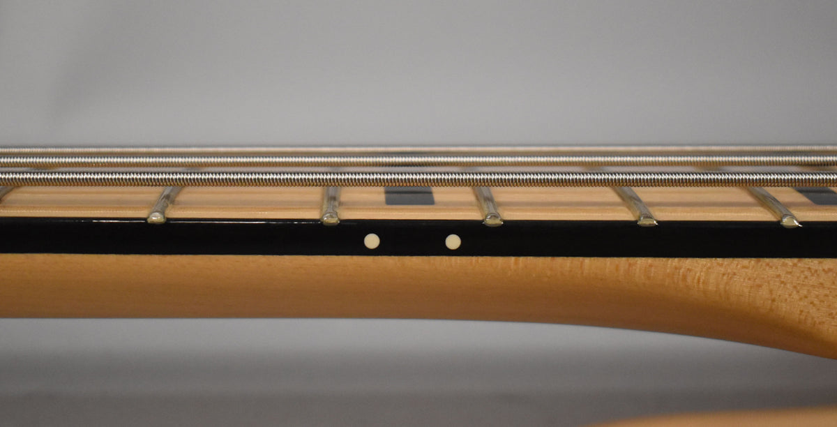 Close-up of the bass neck from the side, showing the maple fretboard with black block inlays and white side dots.