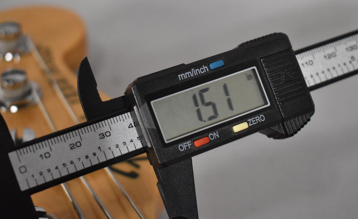 Close-up of a digital caliper measuring the bass's natural finish neck, displaying "1.51" on its screen.