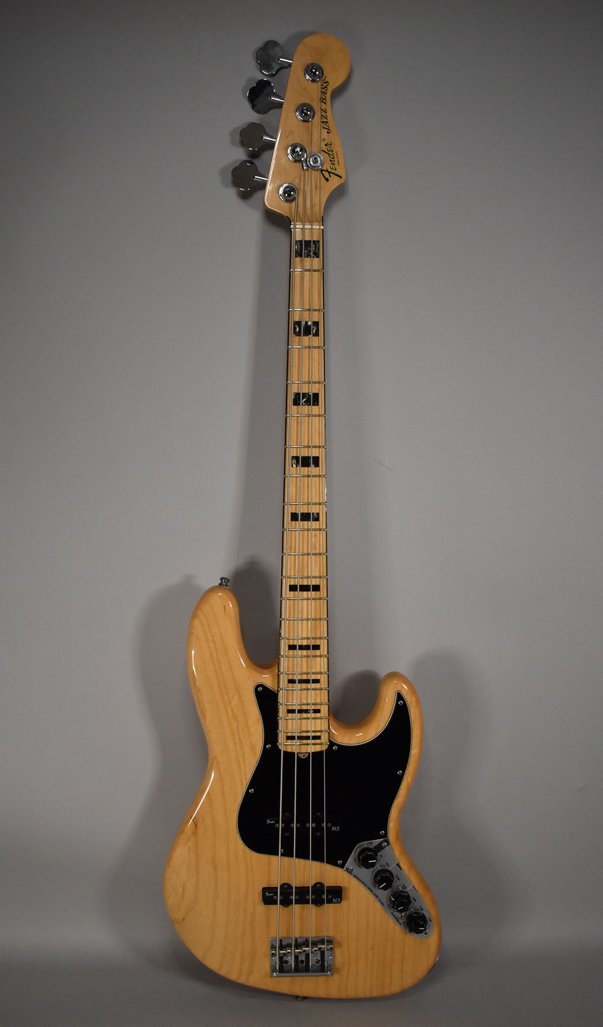 Full-length view of a natural finish bass with a maple neck, black block inlays, black pickguard, and chrome hardware.