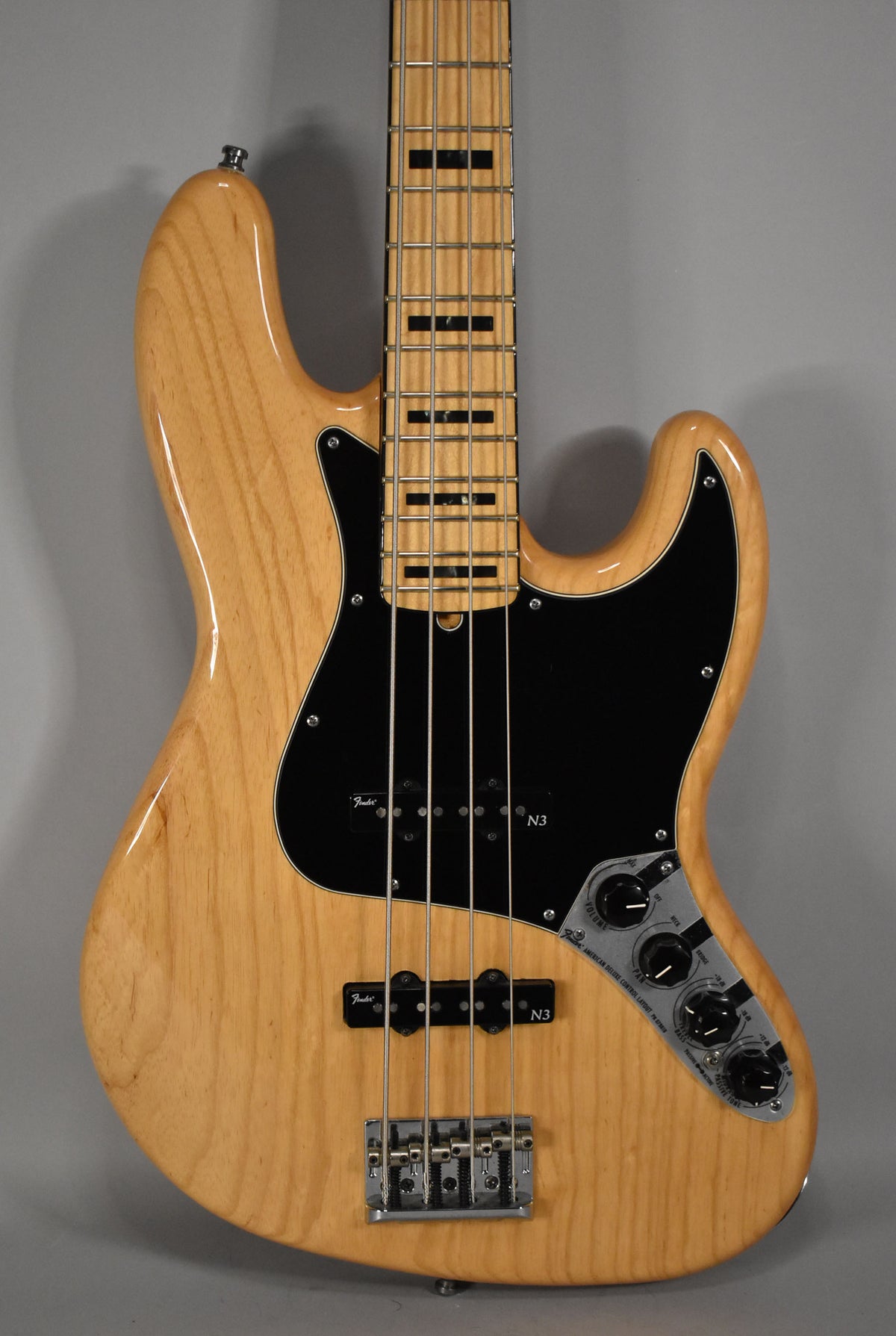 Full front view of a natural finish bass with a black pickguard, two pickups, and a chrome bridge and control plate.
