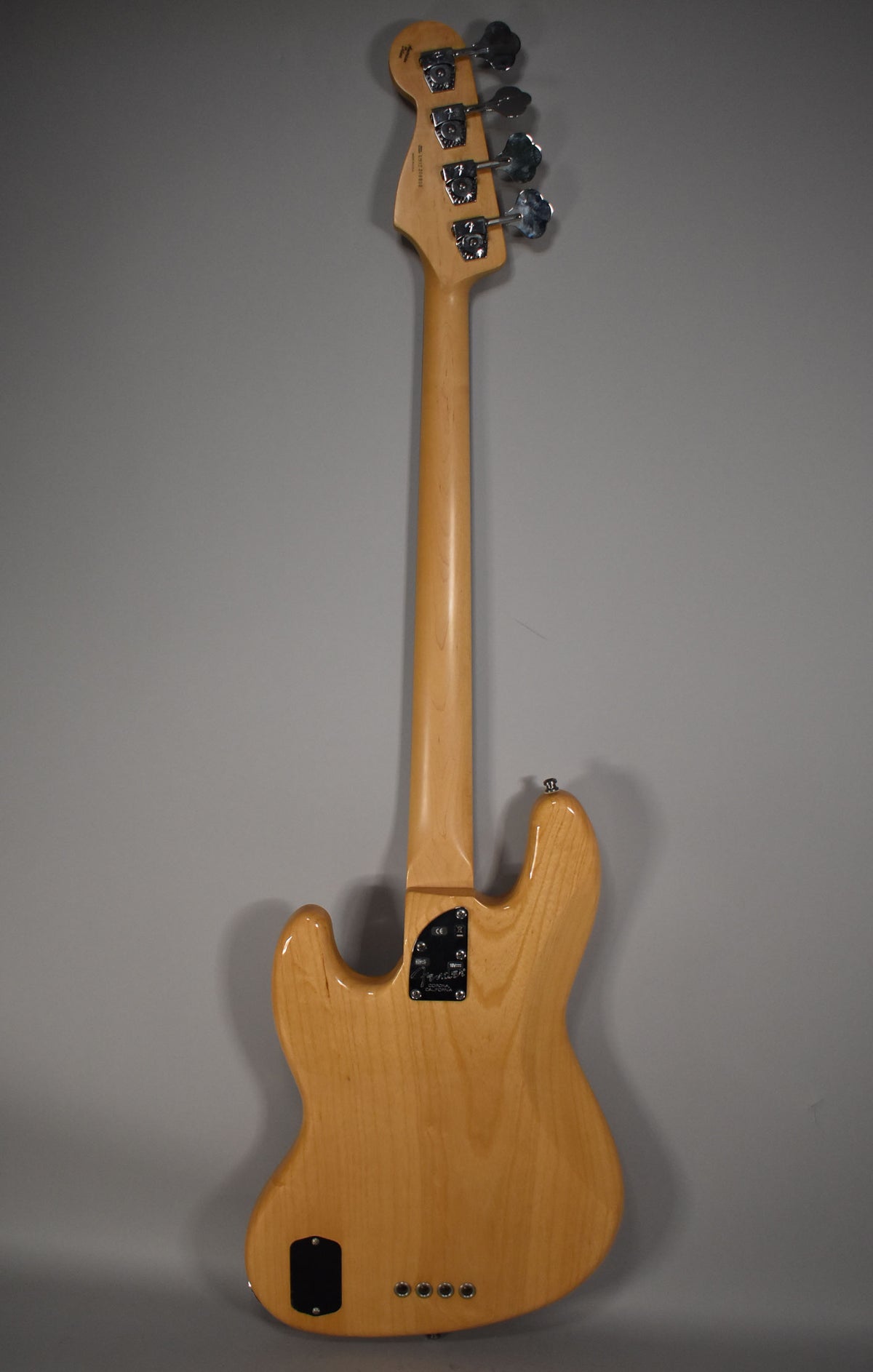 Full rear view of a natural finish bass, showing the light wood body and neck, chrome tuners, and black control plates.