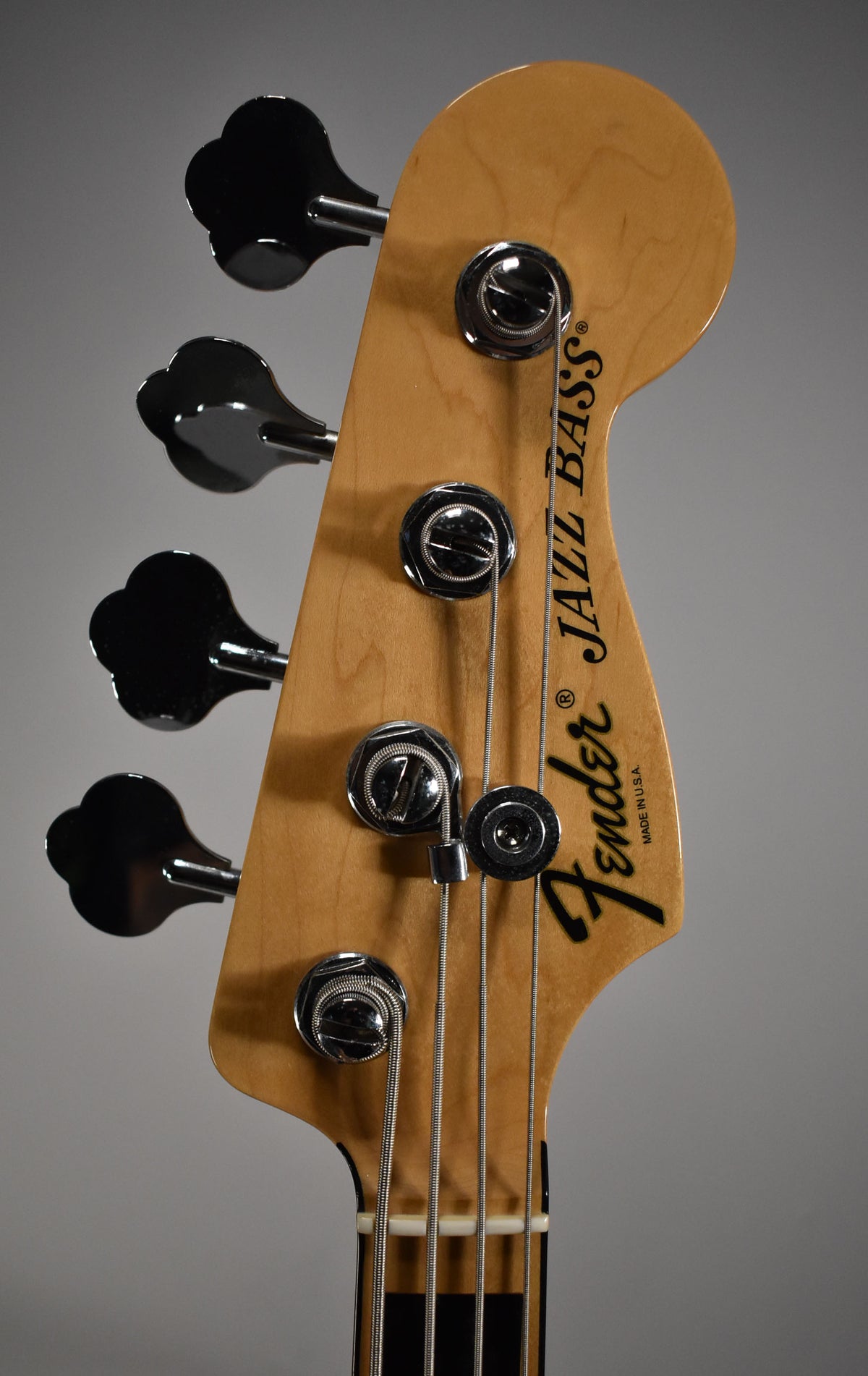 The bass headstock, angled slightly right, shows four black clover-leaf tuners and chrome string trees on a natural wood finish.