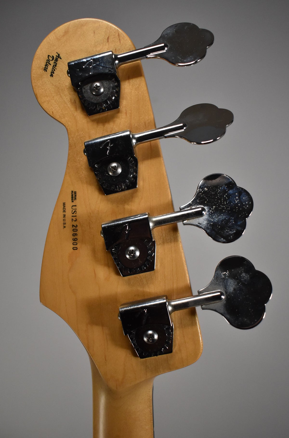 The back of a light wood bass headstock with four chrome clover-leaf tuners, showing some pitting and wear.