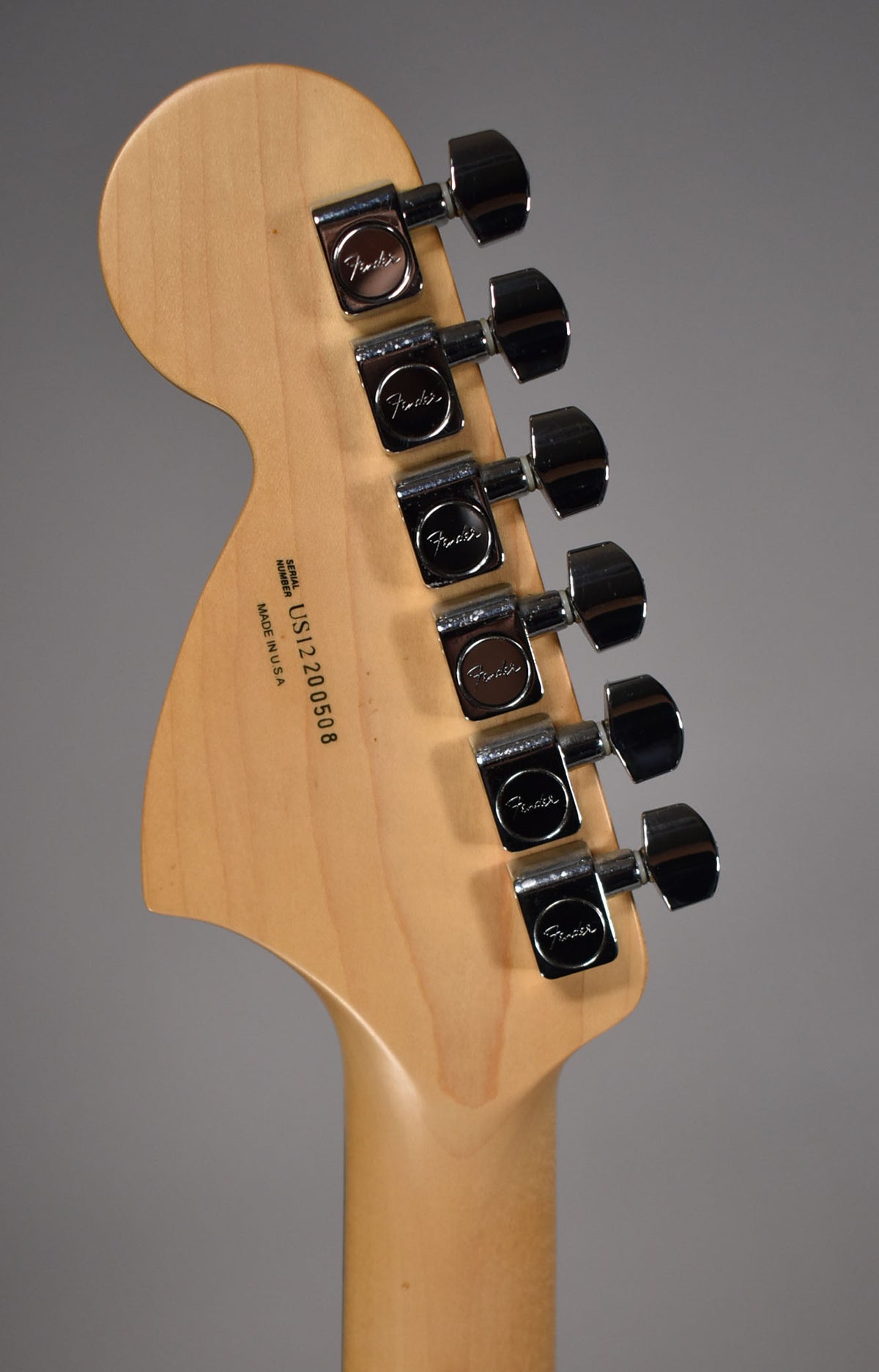 The back of a light maple headstock and neck, with six chrome tuners aligned on the right, and a serial number stamped on the headstock.