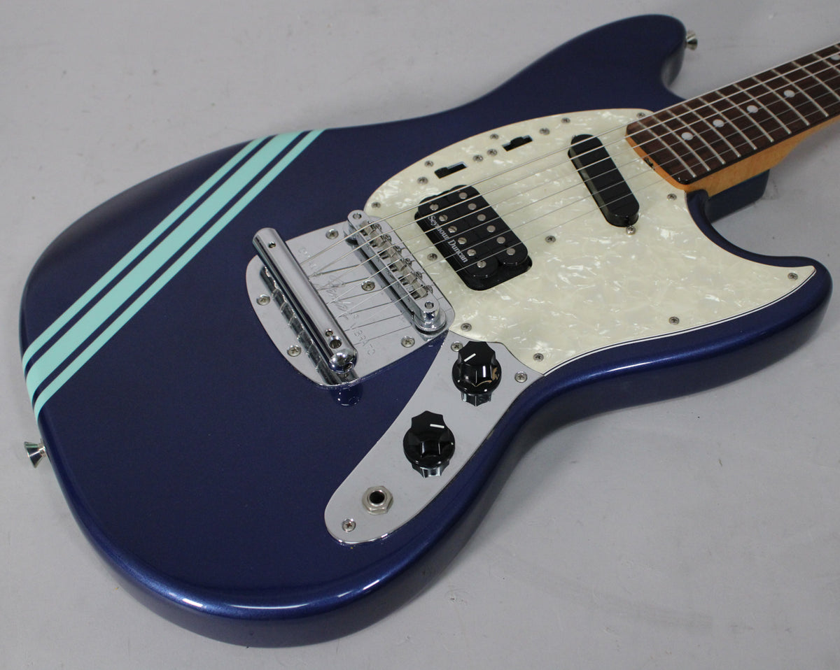 The blue electric guitar's body is angled from the lower left, showing its pearloid pickguard, two black pickups, and chrome hardware.