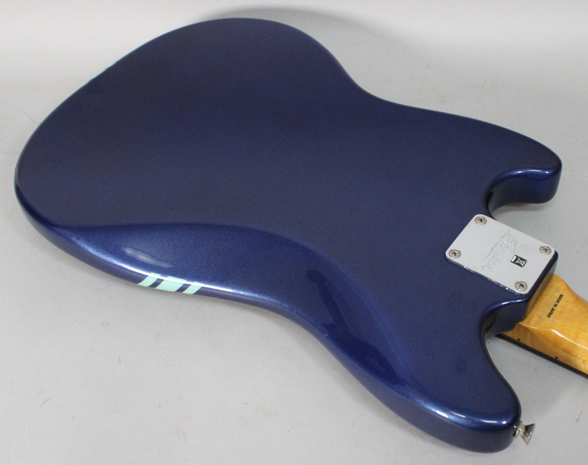 The back of a metallic blue guitar body, angled to show the neck plate and a light blue racing stripe.