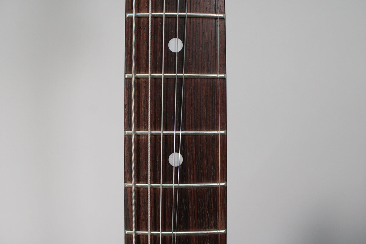 Close-up of the dark rosewood fretboard with silver frets and two white dot inlays, showing light string wear.