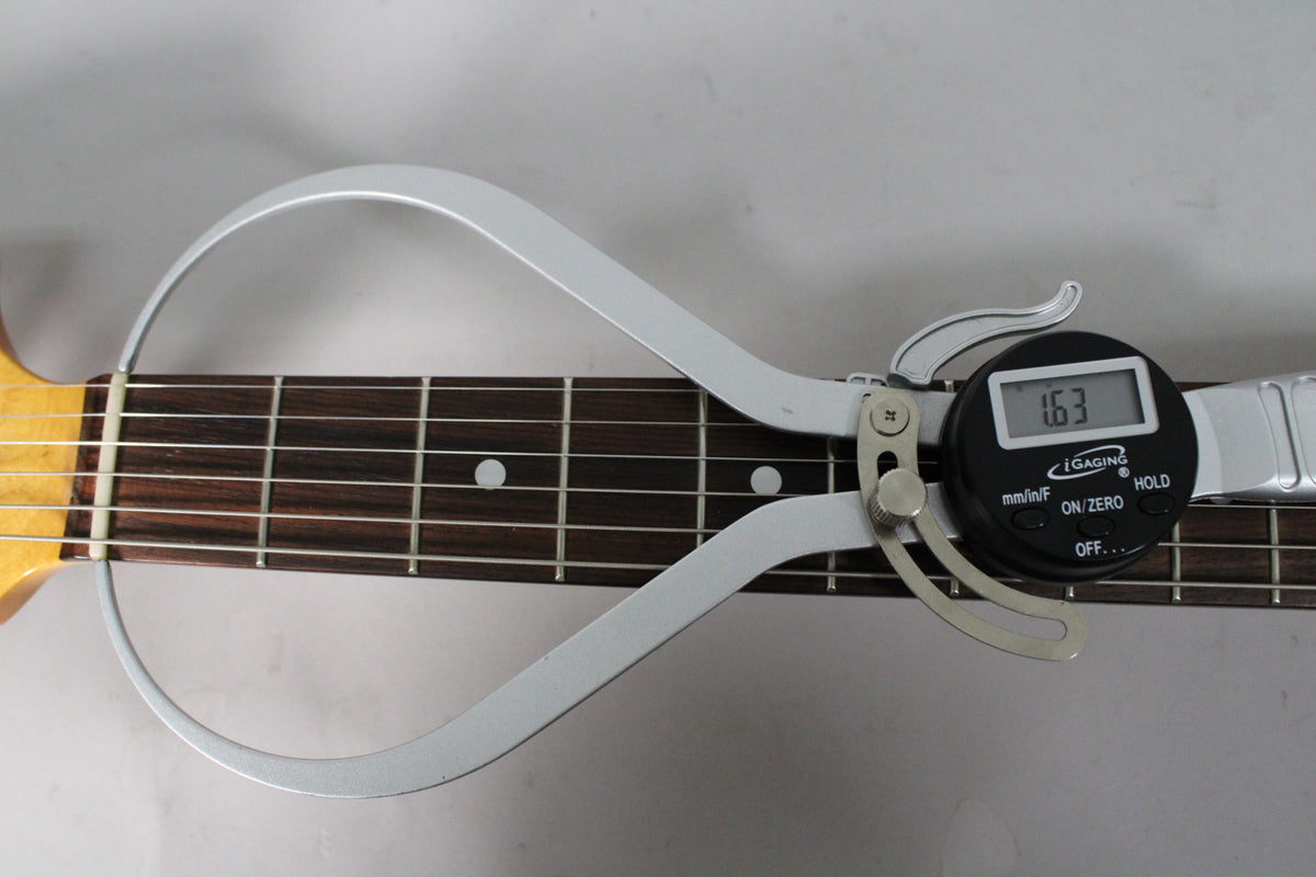 A digital caliper measures the guitar's dark rosewood fretboard, showing a 1.63mm reading on the display.