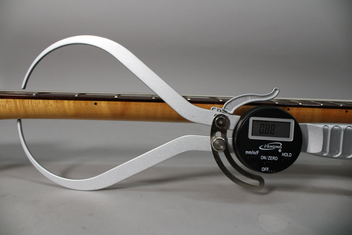 A digital caliper measures the guitar's neck, showing a reading of 0.88, with the light brown neck and dark fretboard visible.