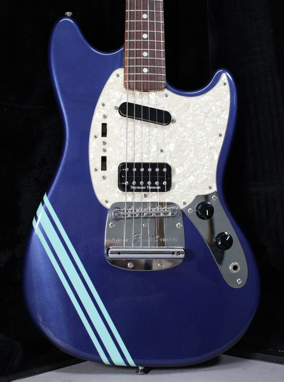 Full body shot of a metallic blue electric guitar with a white pearloid pickguard, two light blue racing stripes, and a chrome vibrato.